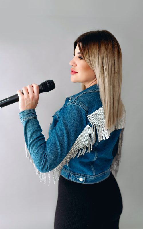 KLAU énekesnő és retro DJ mikrofonnal, farmer kabátban, világos stúdióban