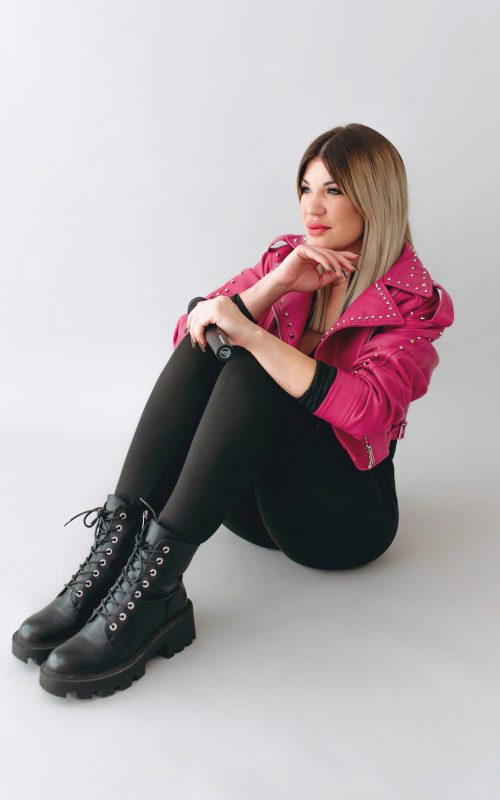 KLAU énekesnő és retro DJ mikrofonnal, földön ülve, fekete ruhában, pink kabátban, világos stúdióban