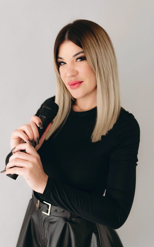 KLAU énekesnő és retro DJ mikrofonnal, sötét ruhában, világos stúdióban